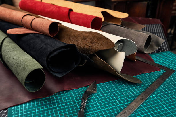 Rolled up samples of textures of genuine leather of different colors on a leather background, on a table with mats and tools for cutting pieces of leather.