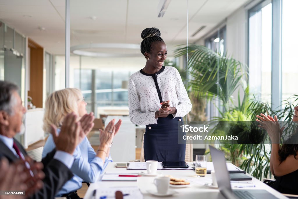 Diverse Group of Executives Applauding African Female CEO Front view of businesswoman in mid 30s smiling as colleagues applaud at conclusion of successful presentation. Leadership Stock Photo