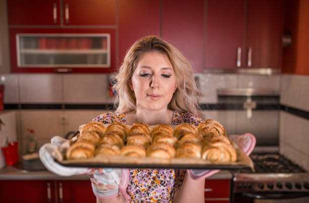 Young housewife holding tray with bun-bread in the kitchen