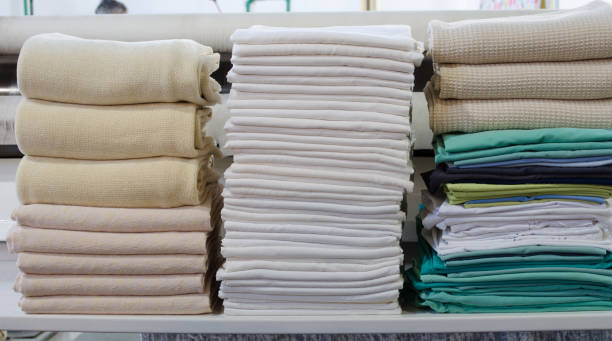 istock Stack of folded clean sheets, surgical clothes  and industrial iron in an industrial laundry. Cleaning and ironing service for hospitals and clinics. 1329135448