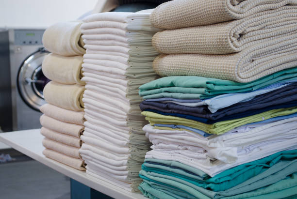 stack of folded clean sheets, surgical clothes  and industrial iron in an industrial laundry. cleaning and ironing service for hospitals and clinics. selective focus. - wassen stockfoto's en -beelden