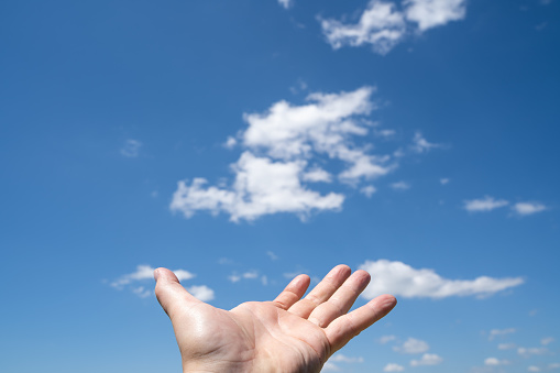 Man holds hand up in the beautiful blue cloudy sky