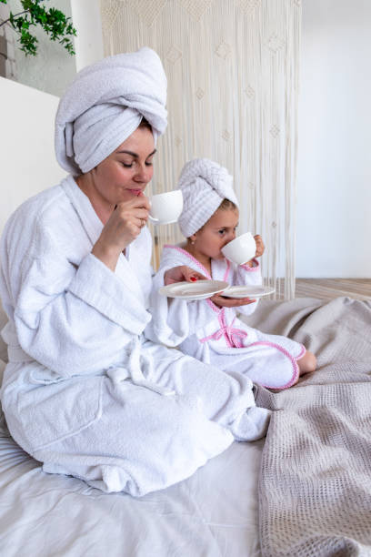 istock Mom and daughter drinking tea while sitting on bed, dressed white terry robes. Nursing communication in the family. 1329159705