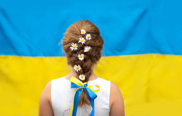 a girl with daisies in a braid and a yellow and blue ribbon against the background of the flag of ukraine. independence day of ukraine, flag day, constitution day - 烏克蘭文化 圖片 個照片及圖片檔