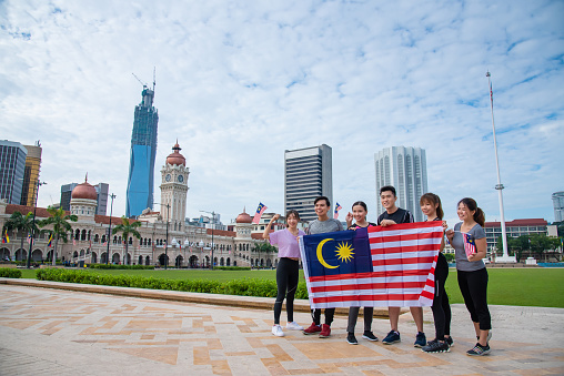 Young Malaysian men and women in sportwear waving Malaysian flags with pride in celebrating the Malaysia Independence Day. High Patriotism Spirit and Independence Day, Hari Merdeka Concepts.