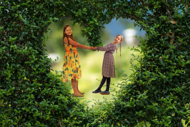 Two children embracing in the garden on a sunny summer day. The outdoor floral decorations in the background suggest a special celebration. One of the children is wearing a white shirt, the other a red and white sleeveless dress. Both children are smiling warmly, radiating a feeling of love and closeness. The photo beautifully depicts the innocence of childhood, friendship and the joy of moments shared in a cozy, festive setting.