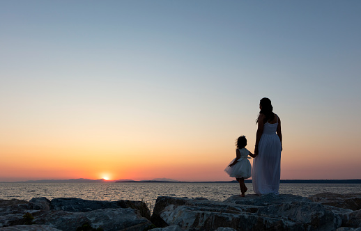 Mom and daughter watch beautiful sea sunset from the pier