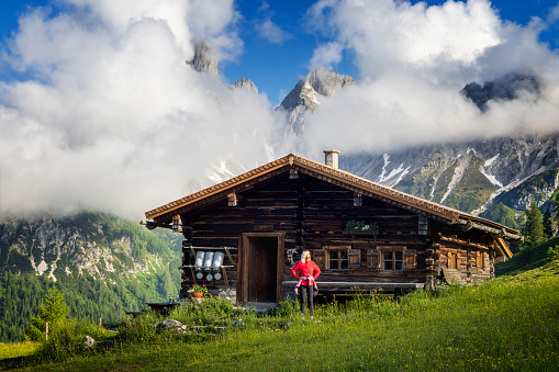 Woman standing in front of alpine hut, Sulzen Alm, Salzburger Land and enjoy the summer day