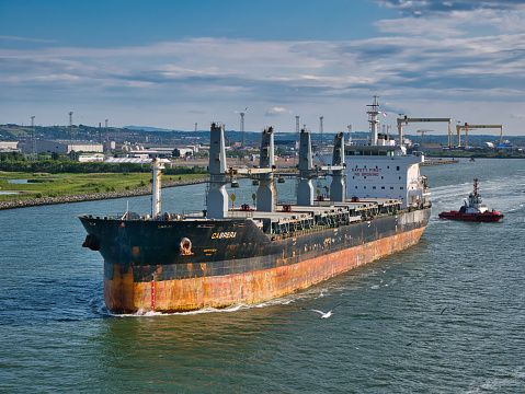 The bulk carrier Cabrera leaving Belfast Harbour in June 2021 on a clear, sunny evening in June 2021. The ship is escorted by the Masterman tug boat.