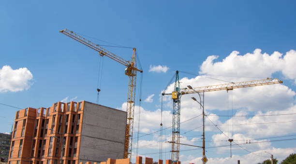 istock Crane and workers at construction site against blue sky. 1329180145