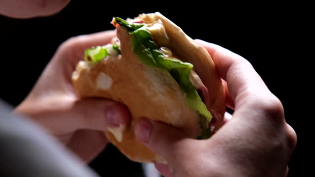 Person is eating sandwich, hands and face are getting dirty. Close-up