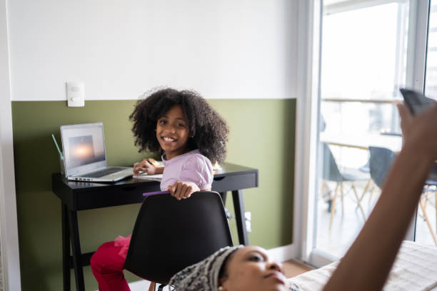 istock Portrait of a girl using laptop while sister's in bed using smartphone at home 1329183196