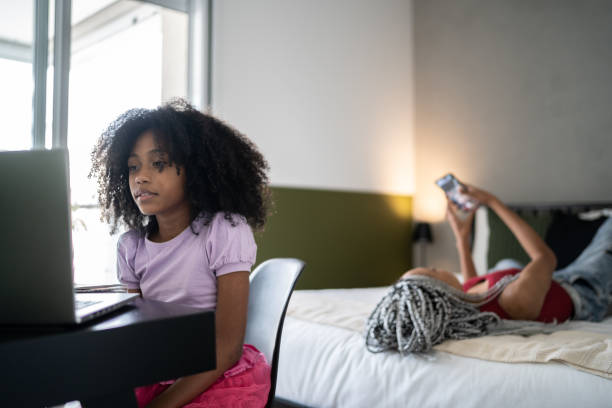 istock Girl using laptop while sister's in bed using smartphone at home 1329183207