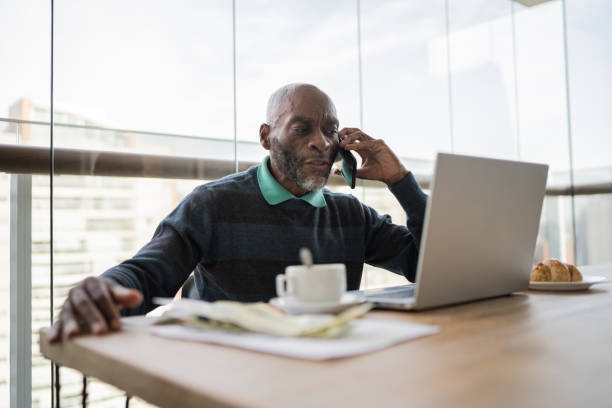 istock Mature man using laptop and talking on smartphone at home 1329183309