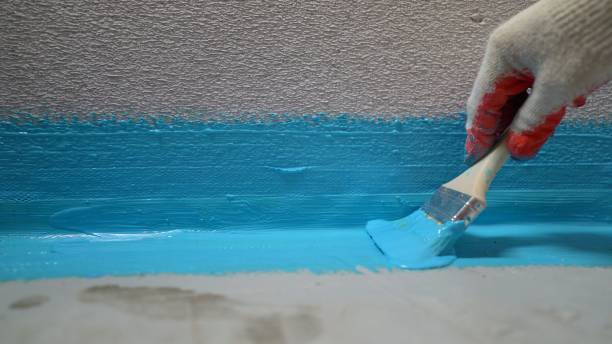 Cover the concrete wall with a cement-polymer waterproofing membrane. Waterproofing with a blue shade brush. The waterproofing coating is blue stock photo