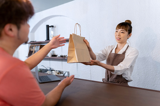 Japanese owner giving food in recycled paper bag to customer.