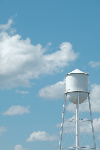 White water tower and blue summer sky with fluffy white clouds and negative space for copy
