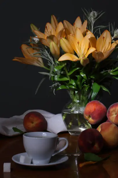 Photo of A bouquet of summer flowers, peaches and a cup of coffee on a dark gray background
