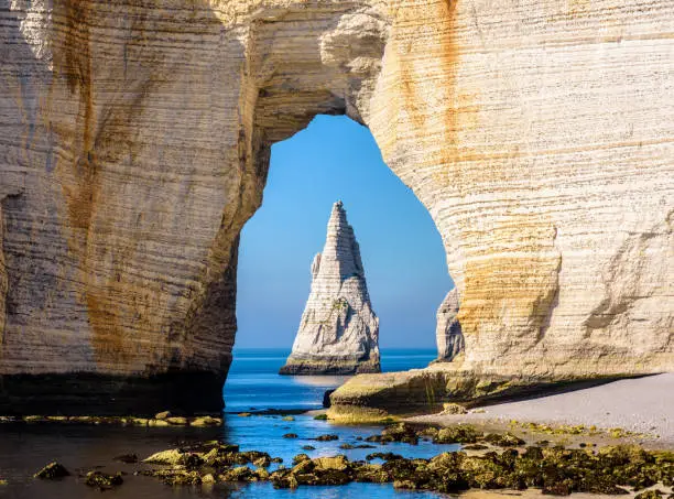 Close-up view of the Needle through the arch of the Manneporte cliff in Etretat, Normandy, a popular french seaside town known for its chalk cliffs, at the end of a sunny day.