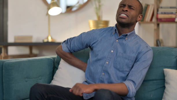 istock Young African Man with Back Pain Sitting on Sofa 1329204569