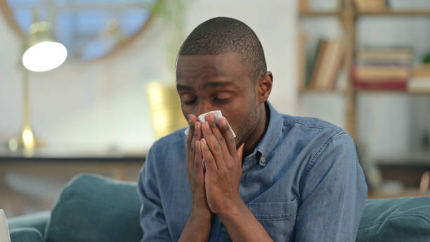 istock Sick Young African Man Sneezing at Home 1329204634