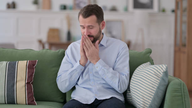 istock Sick Young Man Sneezing Sitting on Sofa 1329204669