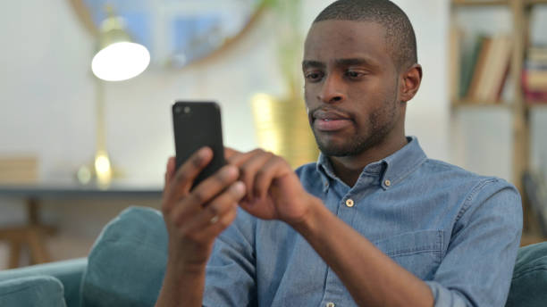 istock Young African Man using Smartphone at Home 1329204804