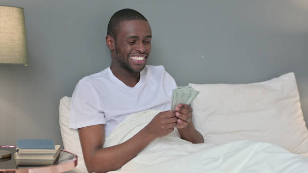 istock Successful Young African Man Counting Dollar in Bed 1329204816