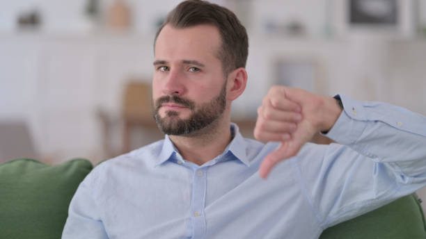 istock Young Man with Thumbs Down at Home 1329204856