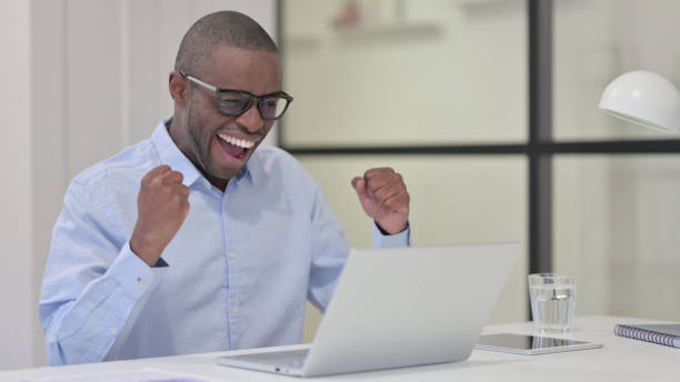 istock Successful African Man Celebrating on Laptop at Work 1329206129