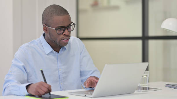 istock African Designer using Laptop and Graphic Tablet for Creating Design 1329206852
