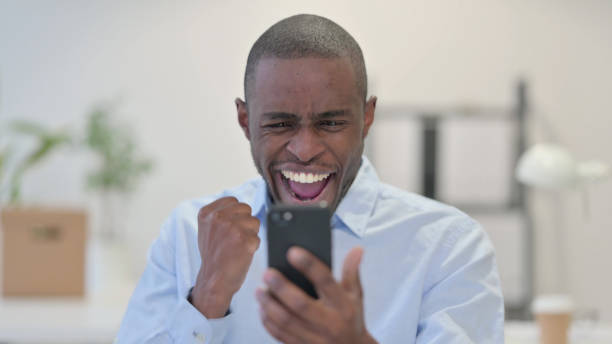 istock African Man Celebrating on Smartphone in Office 1329207389