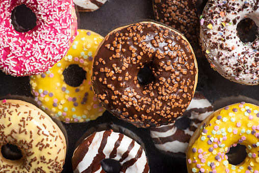 Colorful chocolate covered sweet donuts with sweet sprinkles dessert closeup top view shot