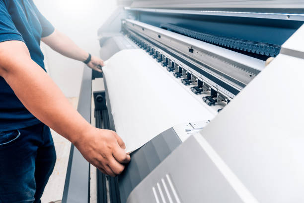 homem segurando material imprimível em um grande formato de impressão plotter.design gráfico e conceito de publicidade. - printing press design computer graphic printer - fotografias e filmes do acervo