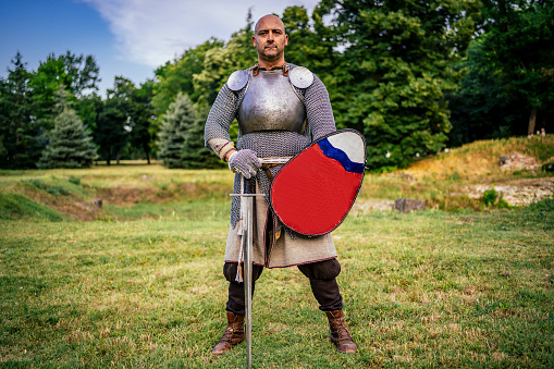 Medieval knight in full chain mail armor with a sword and a shield outdoor