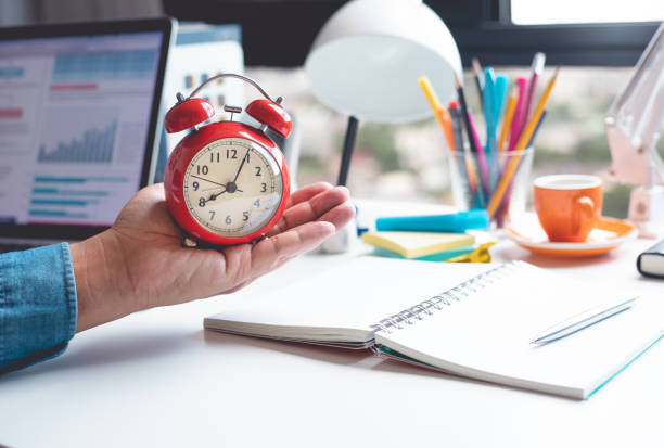istock Time and work concepts with male hand holding alarm clock on desk. 1329211272