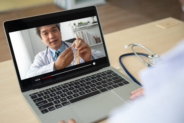 アジアの女性医師は、理学療法を専門とする医師からのビデオチュートリアルを見ています。ビデオ学習、教育、個人開発の概念 - physical therapy ストックフォトと画像