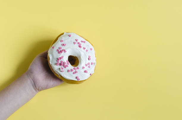 istock A child's hand holding a donut with colored icing on a bright yellow background. Fresh donut on a colored background close-up copy space 1329212853