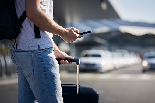 Man holding smartphone and using mobile app against a row of taxi cars. Themes modern technology, carsharing and travel.