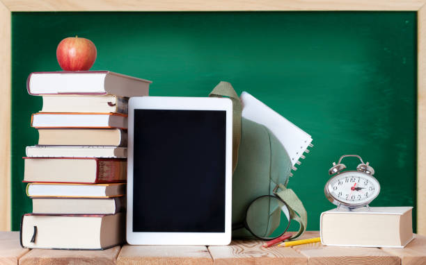 istock Stack of books with red apple, silver clock, digital tablet, color pencils, magnifying glass, white notebook and school bag on the wood table 1329223332