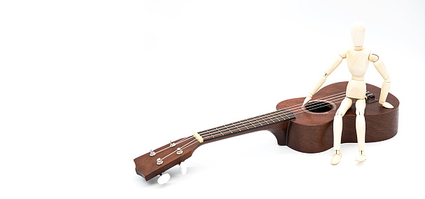 Ukulele acoustic guitar with human mannequin figure . Break time for hobby. Art or musical concept. Brown hawaiian guitar and wooden puppet white background.