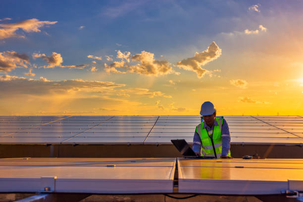 ingénieur utilisant un ordinateur portable sur des panneaux solaires sur le toit au coucher du soleil, un ingénieur travaillant dans une ferme photovoltaïque. écotechnologie pour l’énergie électrique - solar power station solar panel energy electrician photos et images de collection