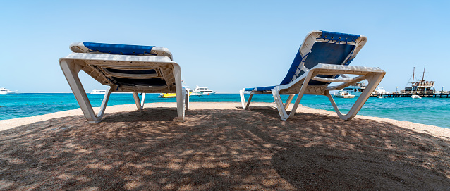 two beach sun loungers in the shade on the shores of the Red Sea against the backdrop of boats and ships in Egypt Hurghada