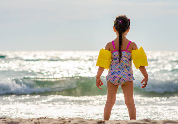 ビーチでスタンド水泳のための腕フリル水着で美しい色の女の子5歳は、水に入りたいです。 - water wings ストックフォトと画像