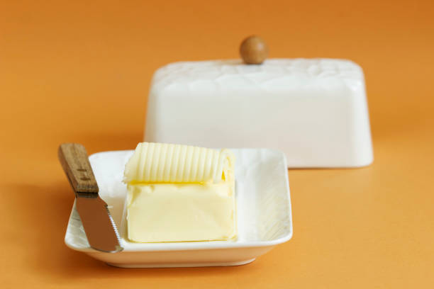 kawałek masła w naczyniu maślanym i nóż na kolorowym tle. - butter dairy product butter dish milk zdjęcia i obrazy z banku zdjęć