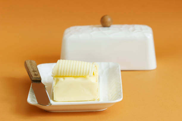 um pedaço de manteiga no prato de manteiga e uma faca em um fundo colorido. - butter dairy product butter dish milk - fotografias e filmes do acervo