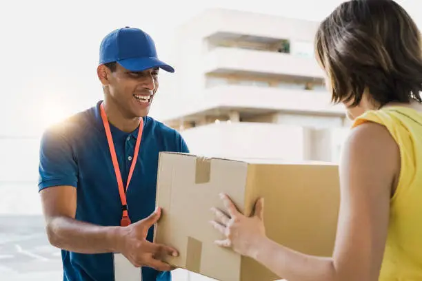 Hispanic courier man shipping cardboard box to customer client for fast delivery - Deliveryman giving package order to customer woman - Focus on guy face