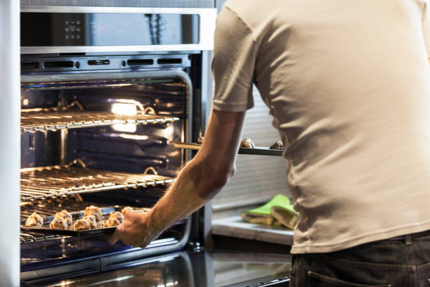 istock Man Putting Dough into the Oven while Baking Chocolate Chip Cookies 1329253843