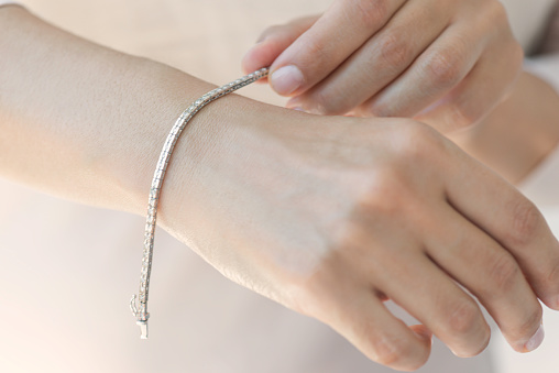 Unrecognizable female is holding a diamond bracelet on her wrist.