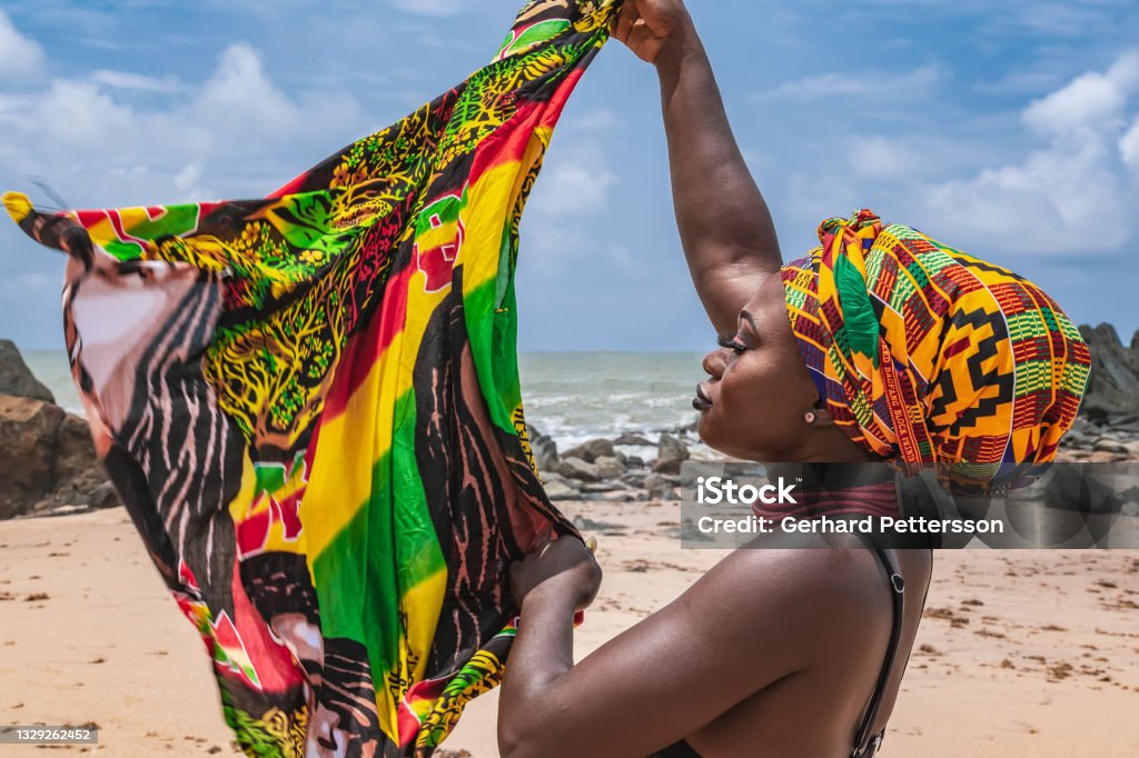 Dancing Ghana woman on the beautiful beach of Axim Dancing Ghana woman on the beautiful beach of Axim, located in Ghana West Africa. Headdress in traditional colors from Africa. Ghana Stock Photo
